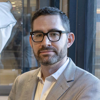 Peter Hyland facing forward, short, dark hair, glasses, button-down shirt, beige jacket.