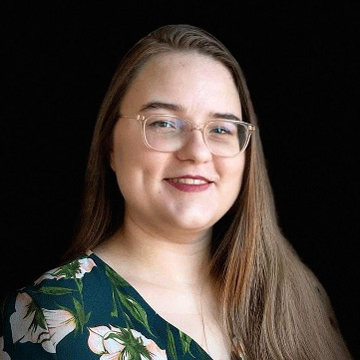 Abigail Meyer facing forward, smiling, wearing glasses, long brown hair, print-fabric shirt