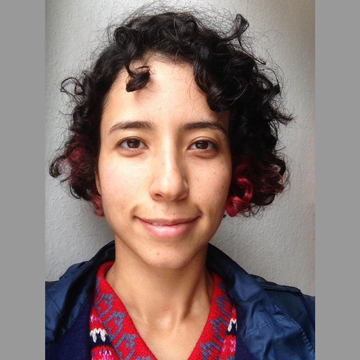 Head-and-shoulders: Nasrin smiling at the camera, dark short curly hair, red and blue shirt