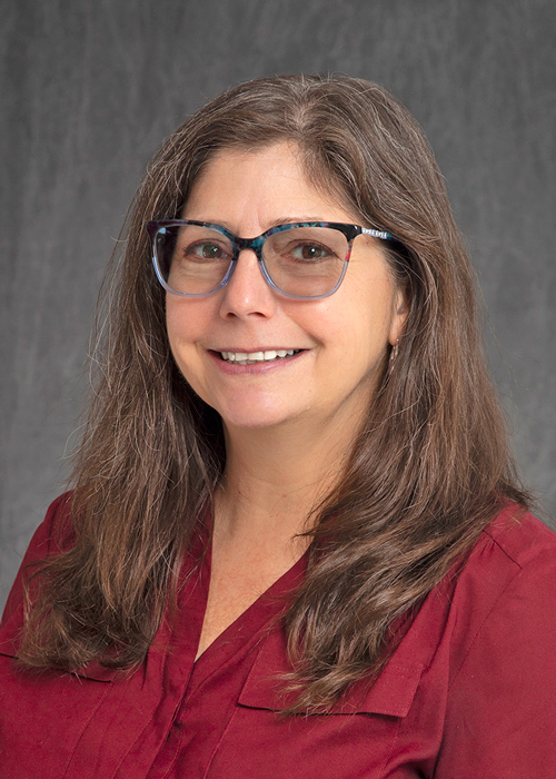 Cindy T. Davis smiling, head-and-shoulders, long brown hair, wearing glasses, maroon top