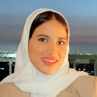 Sahar is facing forward and smiling. She wears a white head scarf and a beige top.