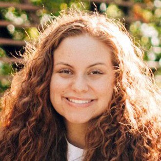 Bailey is facing forward and smiling. She has long curly hair.