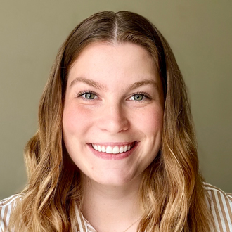 Susan is facing forward and smiling. She has brown wavy hair and wears a brown shirt.