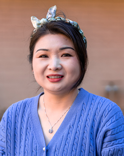 Panpan Yang is facing forward and smiling. She wears a bow in her dark hair with a blue top..