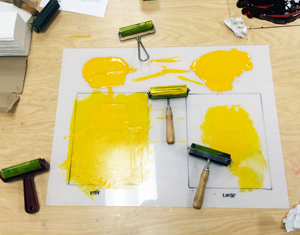 Close up of workshop materials - yellow paint, rollers, paper