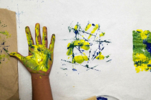 Image of a student participants hand with palm side covered in two paint colors and the image of the handprint next to it on paper.